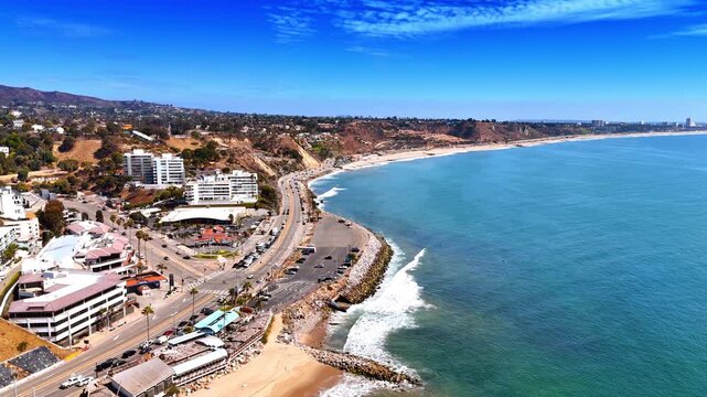 Footage along the coast of the Pacific Ocean. Multiple cars ride by the road along the shore of Malibu, Los Angeles County, California, USA.