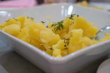 Boiled potatoes with fresh dill served in a white ceramic bowl on a dining table.