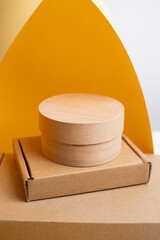 Eco friendly cardboard boxes and round kraft packaging on yellow and gray background. Minimal composition for branding, product presentation, or cosmetic packaging mockup.