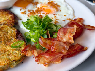 Crispy bacon with fried eggs and green onion closeup. Savory breakfast detail, freshness, and delicious texture.