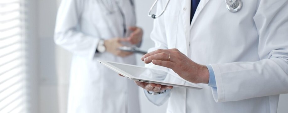 Doctors working together on medical records while a healthcare professional uses a digital tablet for patient data management in a technology-driven clinic - Powered by Adobe