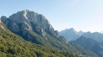 Fototapeta premium Majestic mountain peak rises above lush green forest under a clear blue sky, showcasing the natural beauty and serenity of the rugged wilderness landscape.