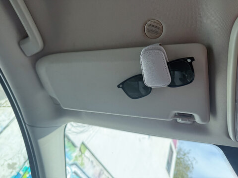 Car sun visor with sunglasses and air freshener. Daily driving, minimalism and lifestyle convenience through personal accessories and travel routine.