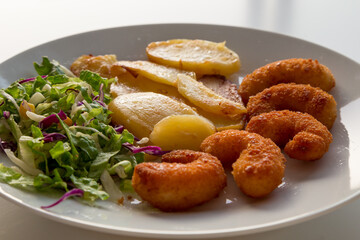 Piatto con gamberi impanati fritti, patate al forno e insalata mista