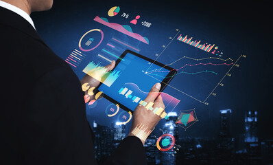 A businessman engages with a tablet displaying vibrant data visualizations and graphs in a stylish urban environment at night. Impute