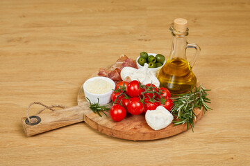 Mediterranean charcuterie board with prosciutto, mozzarella, cherry tomatoes, olives and olive oil on wooden cutting board. Perfect for appetizer or party food.