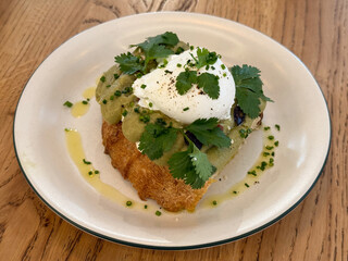 Close-up avocado toast with poached egg and herbs on plate. Healthy breakfast, modern cuisine and fresh culinary aesthetics with natural ingredients
