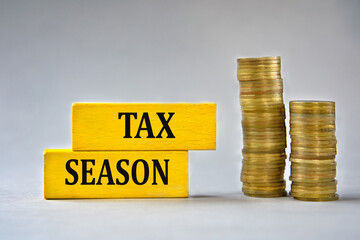 TAX SEASON - words on yellow wooden blocks on the background of stacks of coins