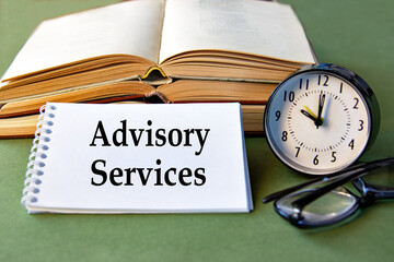 ADVISORY SERVICES text notebook with alarm clock, glasses and books on a green background