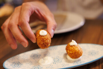 Hand picking up traditional spanish croqueta from plate. Hand lifting a fried croquette with white sauce from a decorative plate