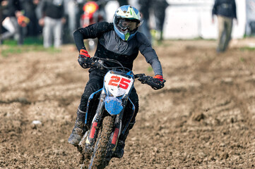 Professional motocross rider speeding on muddy off road track during competition