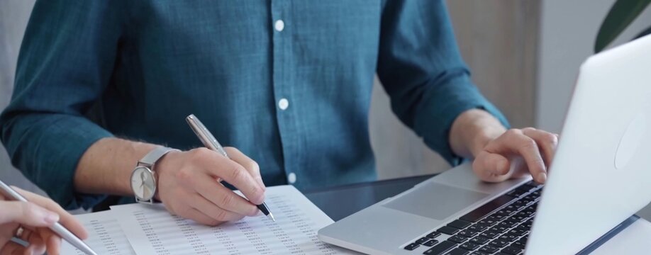 Close-up of a calculator with a male professional auditor working with spreadsheets and a laptop on the background. Business audit and taxes