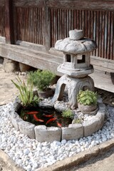 A stone lantern and miniature pond with goldfish, surrounded by plants and white pebbles