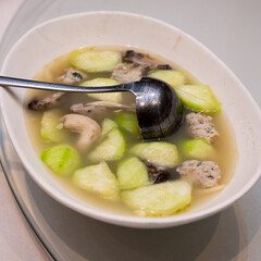 Clear broth soup with gourd slices, meatballs, and mushrooms served in a white bowl, accompanied by a ladle on the side