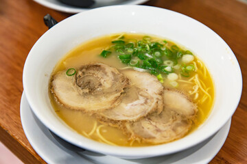 Bowl of traditional tonkotsu ramen with chashu pork slices, green onions and creamy broth served in white bowl on restaurant table