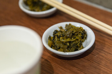 Small white dish filled with chopped pickled mustard greens on wooden table, served as traditional side dish in Asian cuisine