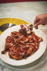 Hand serving Cantonese style roast duck from large white platter at banquet table, golden crispy skin and juicy slices of duck meat visible