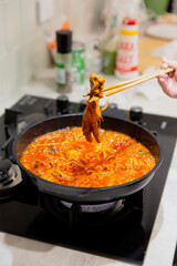 Homemade spicy Korean chicken feet stew boiling in red chili broth, hand holding chopsticks lifting piece from bubbling pot on kitchen stove