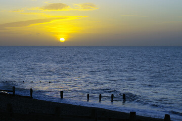 A golden sunset over the ocean with wooden posts along the beach.