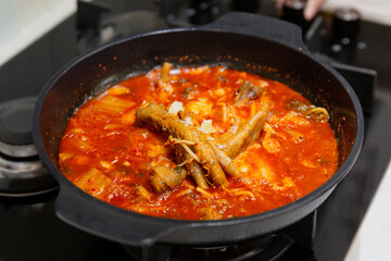 Boiling pot of spicy Korean stew with visible chicken feet and vegetables in red broth, placed on kitchen stove during home-cooked meal preparation
