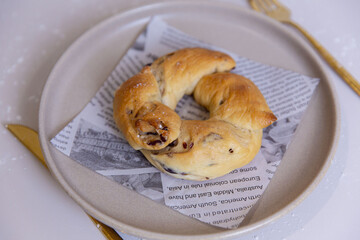 Rustic twisted bread ring with dried cranberries, golden brown crust and visible fruit bits, arranged on printed paper on ceramic plate