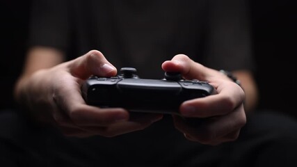 Close-up of hands holding a black game controller, focused on intense gameplay. Low-key lighting, dark background, gaming concept. - Powered by Adobe
