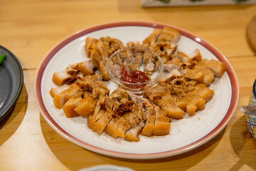 Sliced pork belly arranged in circular pattern on a white plate with spicy dipping sauce in center, garnished with fried garlic and sesame seeds
