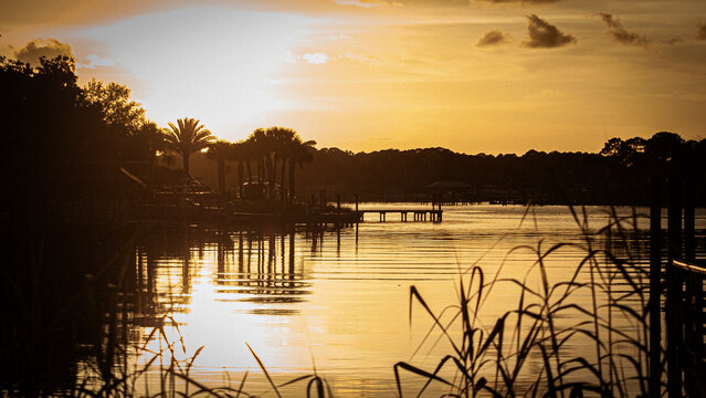P&ocirc;r do sol vibrante com o c&eacute;u em tons de laranja, roxo e dourado, criando uma atmosfera calma enquanto o sol se aproxima do horizonte. Silhuetas naturais acrescentam profundidade e sensa&ccedil;&atilde;o de tranqui