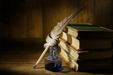 Old antique books with feather and ink bottle on old wooden table. Feather for calligraphy, old...