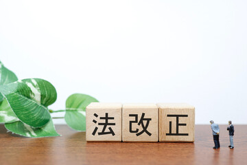 法改正を象徴する木のブロックとビジネスマンのミニチュア。