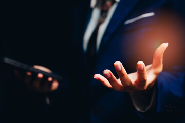 Business professional in suit presenting innovative ideas with hand gesture, technology interface in dark environment