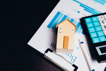 Wooden house model on business report with calculator and pen representing property investment and financial planning concepts