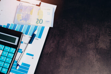 Calculator, financial report, euro bill, stationery tools, and business documents on a dark wooden...