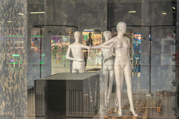 Mannequins displayed in shop window with reflections of mall interior and empty retail setup. Concept of fashion retail, storefront visuals, display design