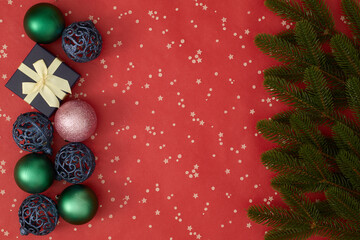 Christmas tree branches, baubles, and a blue gift box with a golden ribbon on a red background, festive holiday composition