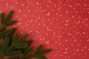 Christmas flat lay: green pine branches on red background with white stars and dots. Festive...