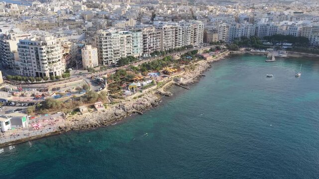 Cinematic drone shot sweeps over the iconic Sliema promenade, capturing luxury high-rises and the deep blue Mediterranean sea along the vibrant Maltese coastline