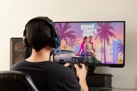 A young male gamer holding a xbox controller and using gamer earphones watching a screen with grand Theft auto 6