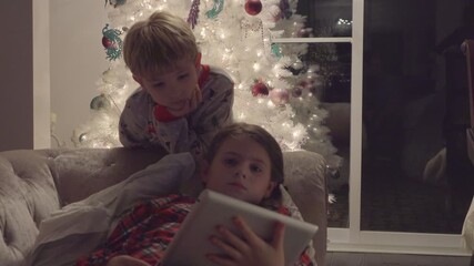 Happy children watching a video on a digital tablet together in a cozy, Christmas decorated living room at home
