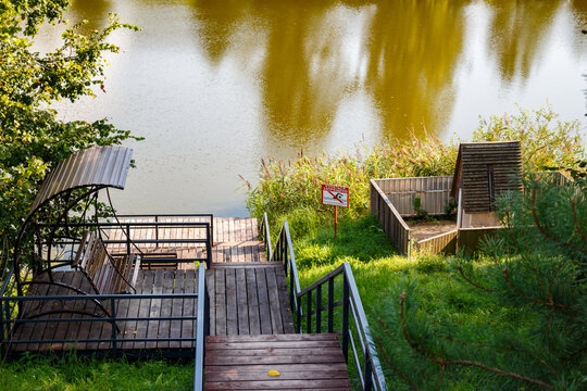 A scenic wooden viewing deck with a covered swing by a serene pond, surrounded by lush greenery, perfect for relaxation