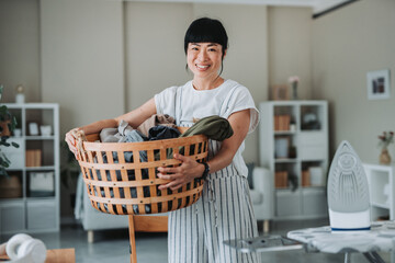 Housewife carrying laundry basket and smiling at home