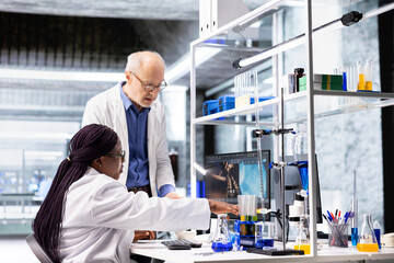 Colleagues in research lab analyzing flasks and chemical samples for experiment. Collaborative workspace highlighting innovation in biochemistry, nanotechnology for medical research.