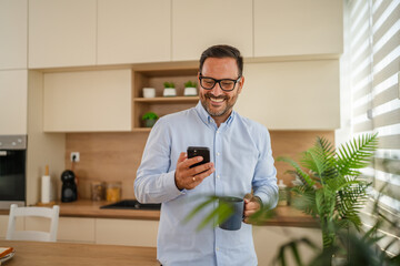 Happy man checking smart phone in modern kitchen