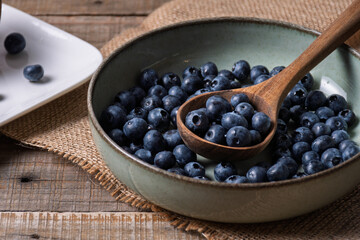 Wooden spoon with blueberries inside a ceramic bowl.