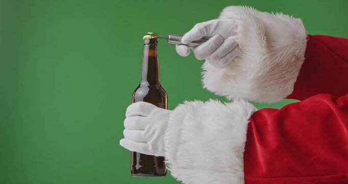 Santa Claus hands in a red suit with a white fur cuff and gloves opens a dark bottle of beer, isolated on a green background. Perfect for Christmas banners, cards, and holiday advertising. Slow motion