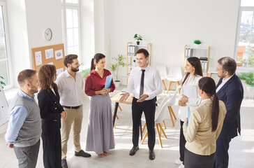 Diverse small business team standing brainstorming on project, planning day in office co working space, discussing new teamwork, working on cooperation, male leader talking to happy colleagues