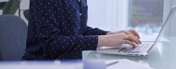 A female accountant with blue dotted blousy is using a laptop computer and calculator to calculate taxes at a glass desk in the office