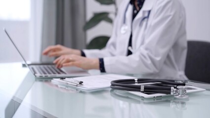 Stethoscope and clipboard are lying on the glass table while doctor woman is using tablet computer on the glass table. Medicine concept