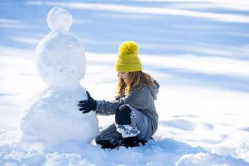New Year holiday. Child playing with snowman in snow field. Kids winter activity. Kids winter...