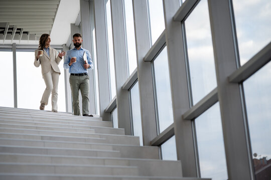 Business colleagues walking downstairs while talking on coffee break